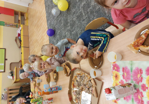 Dzieci siedzą przy stole i jedzą pizze
